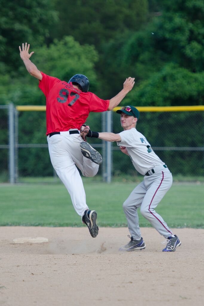 Baseball player slides into base, arms raised, while baseman attempts to tag him; green field, overcast sky.