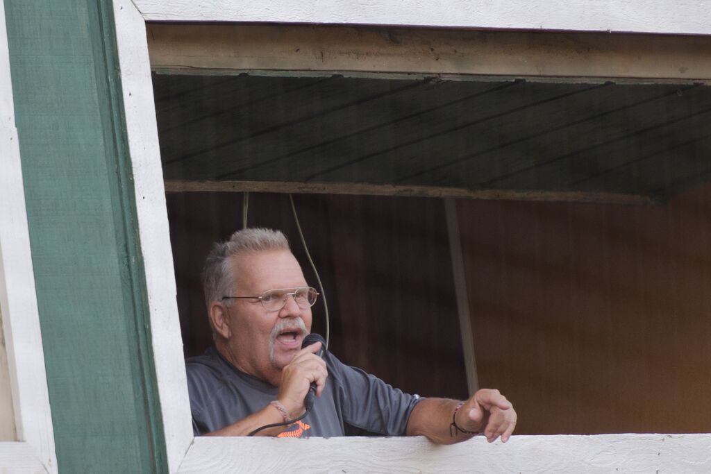 Man with glasses and microphone speaking from a wooden window frame.