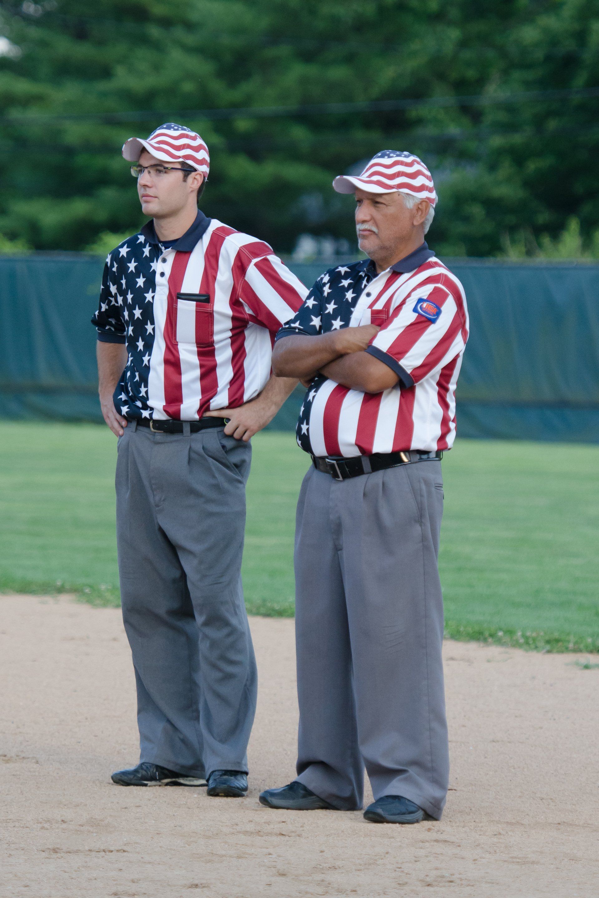 Two baseball umpires wearing patriotic shirts and hats, standing on a field.
