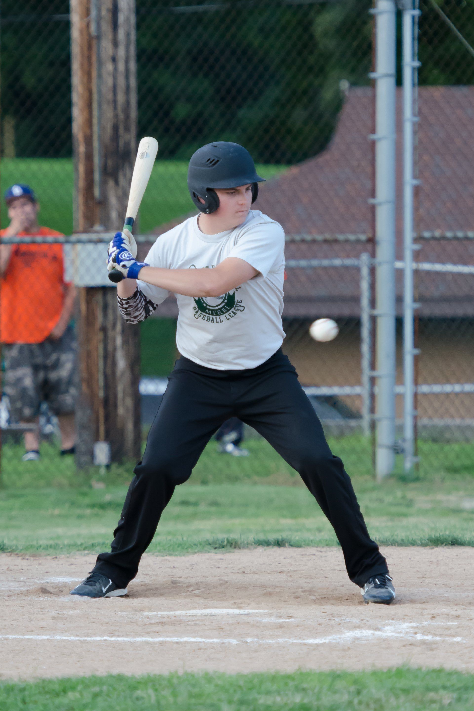 Baseball player in batting stance, ready to hit a pitch. Dark helmet, black pants, white shirt, outdoor field.