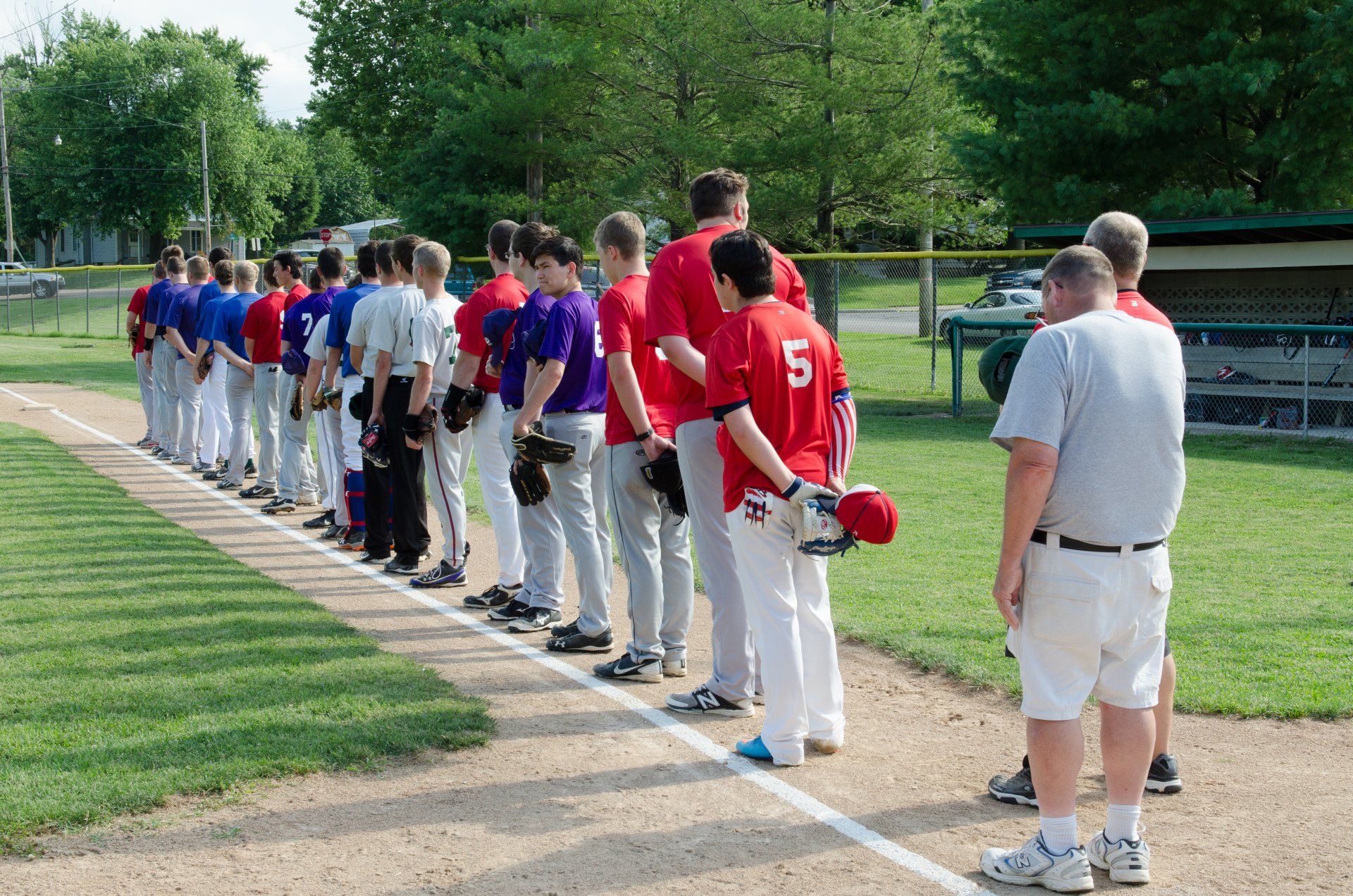 Baseball teams lined up on the field, wearing red, blue, and purple uniforms, preparing for a game.