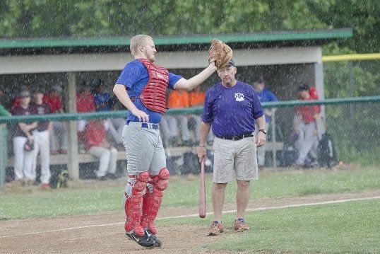 Baseball catcher in red gear, high-fiving a coach on the field during the rain.