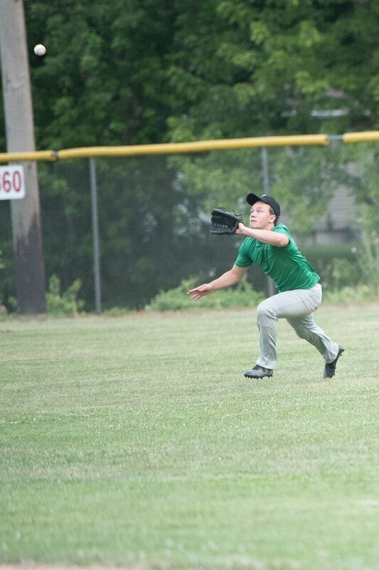 Baseball player in green shirt catches a ball in the outfield.