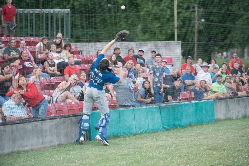Baseball catcher jumping to catch ball in front of a crowd in red bleachers.