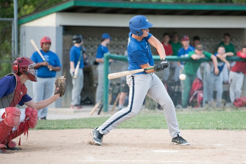 Baseball batter swings at a pitch during a game; catcher crouches.