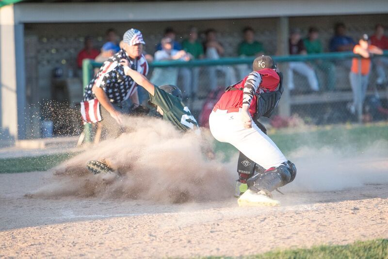 Baseball player sliding into home plate, dust cloud, umpire signals out.