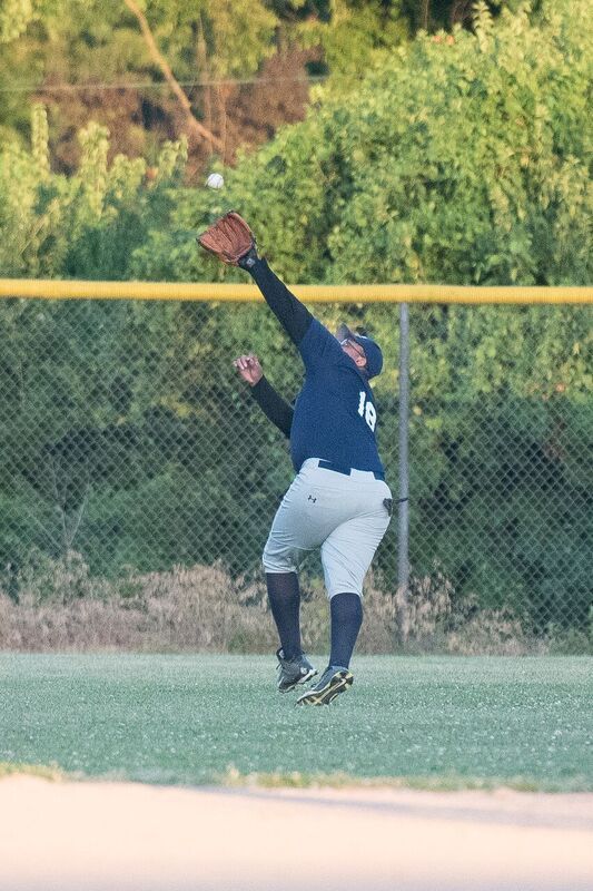 Baseball player in mid-air, reaching for a ball in a game; blue and gray uniform, outdoors.