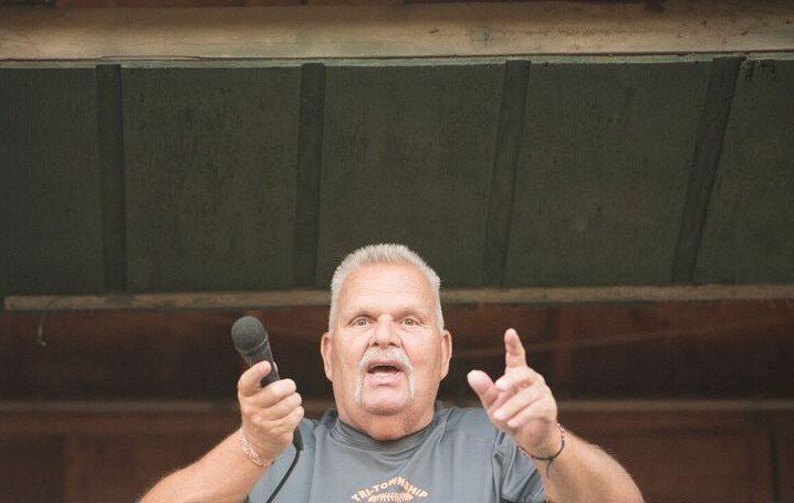 Man with microphone points upward, standing outdoors.
