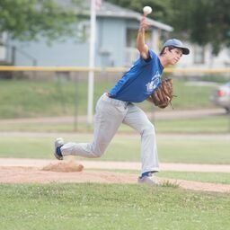A baseball player in blue shirt throws a pitch on a field; light-colored pants, glove visible.