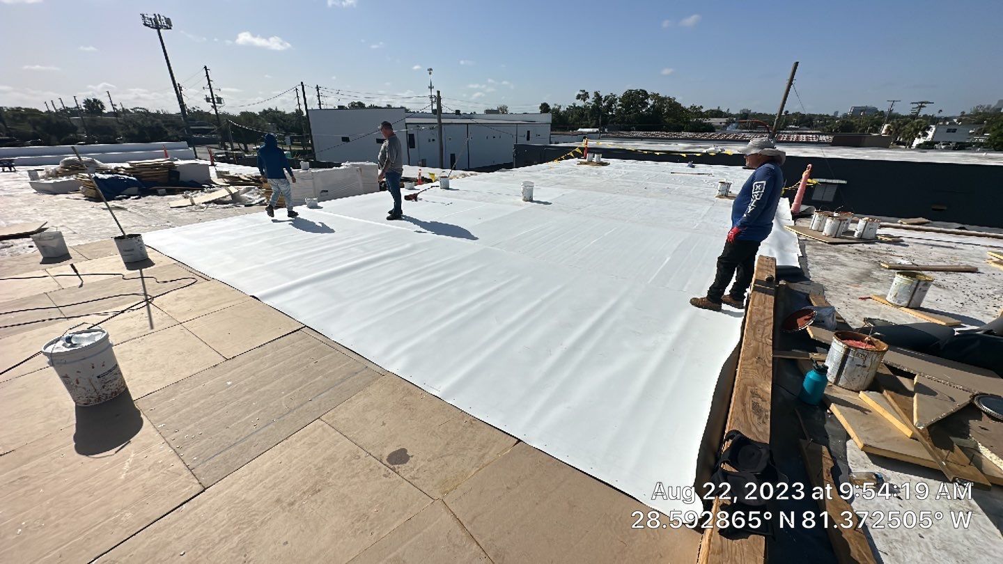 Technician applying single ply roofing material on a flat roof. Commercial roofing project in progress 
