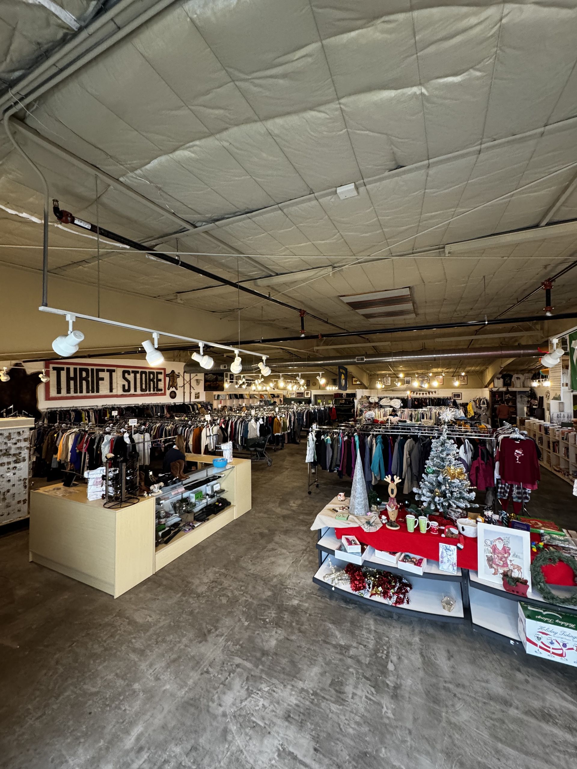 Interior of a thrift store with clothing racks, a checkout counter, and festive holiday decorations.