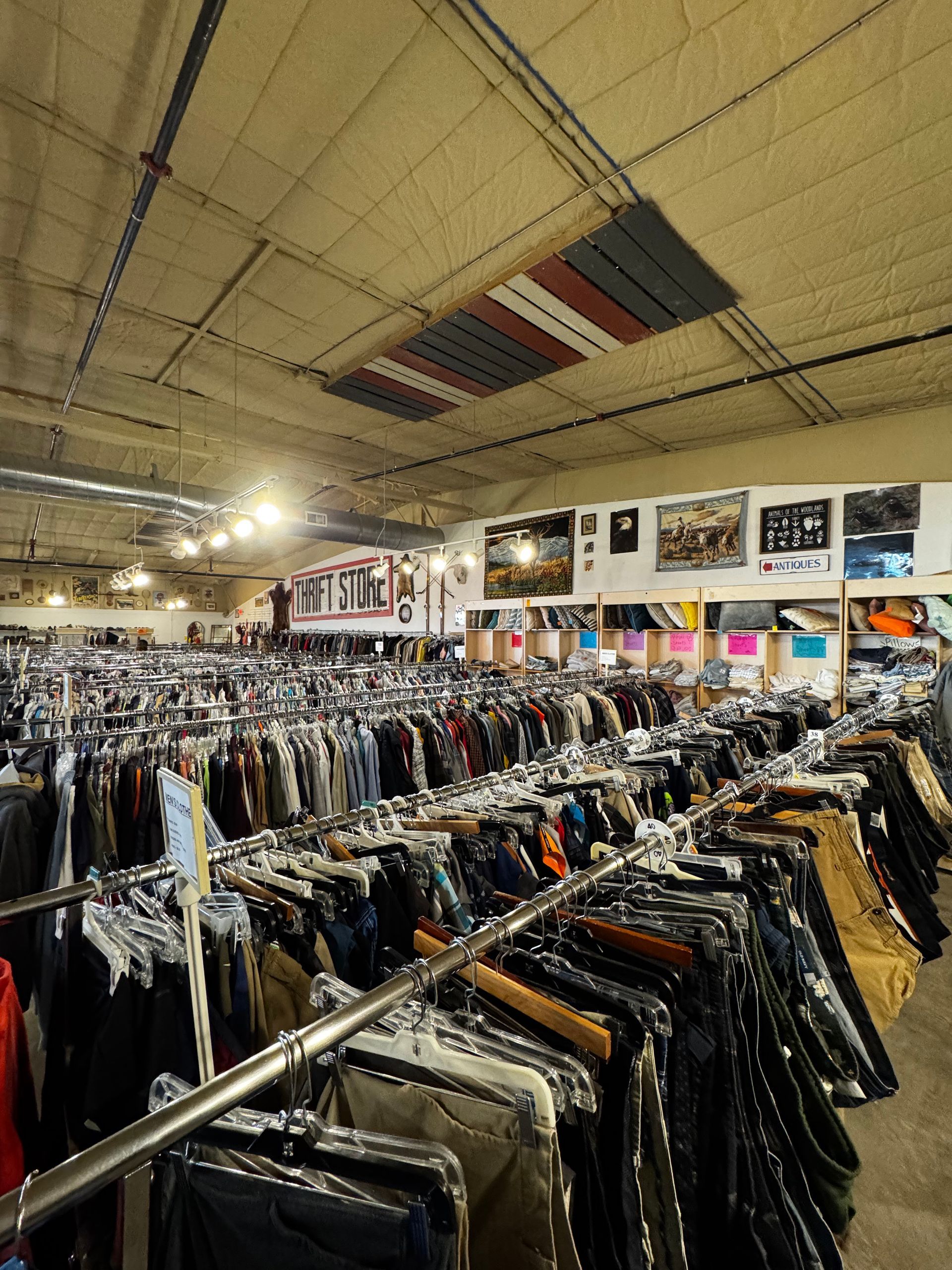 Rows of clothing racks inside a brightly lit thrift store, under an American flag ceiling decoration.