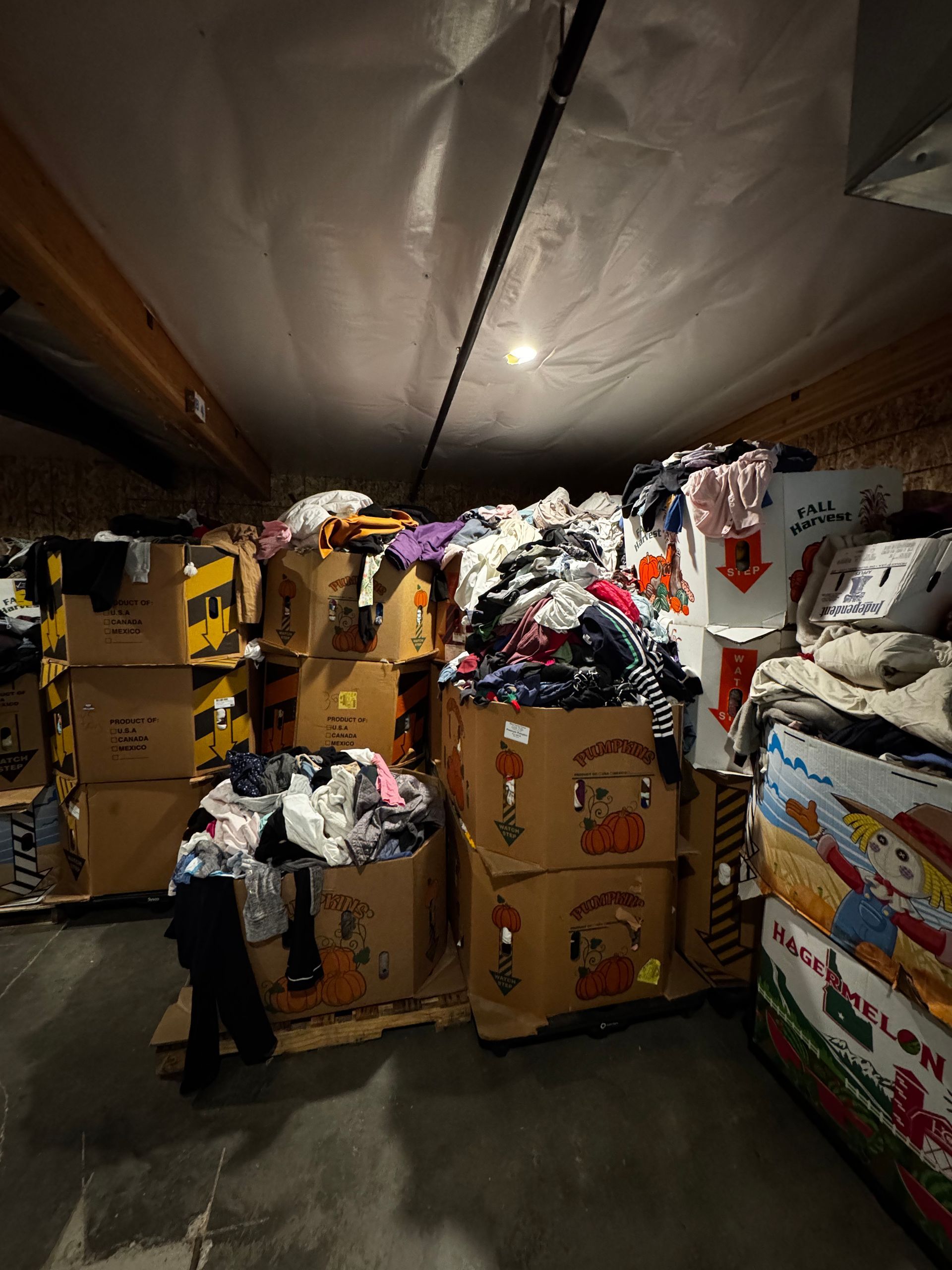 Boxes overflowing with clothes in a storage space under a low ceiling.