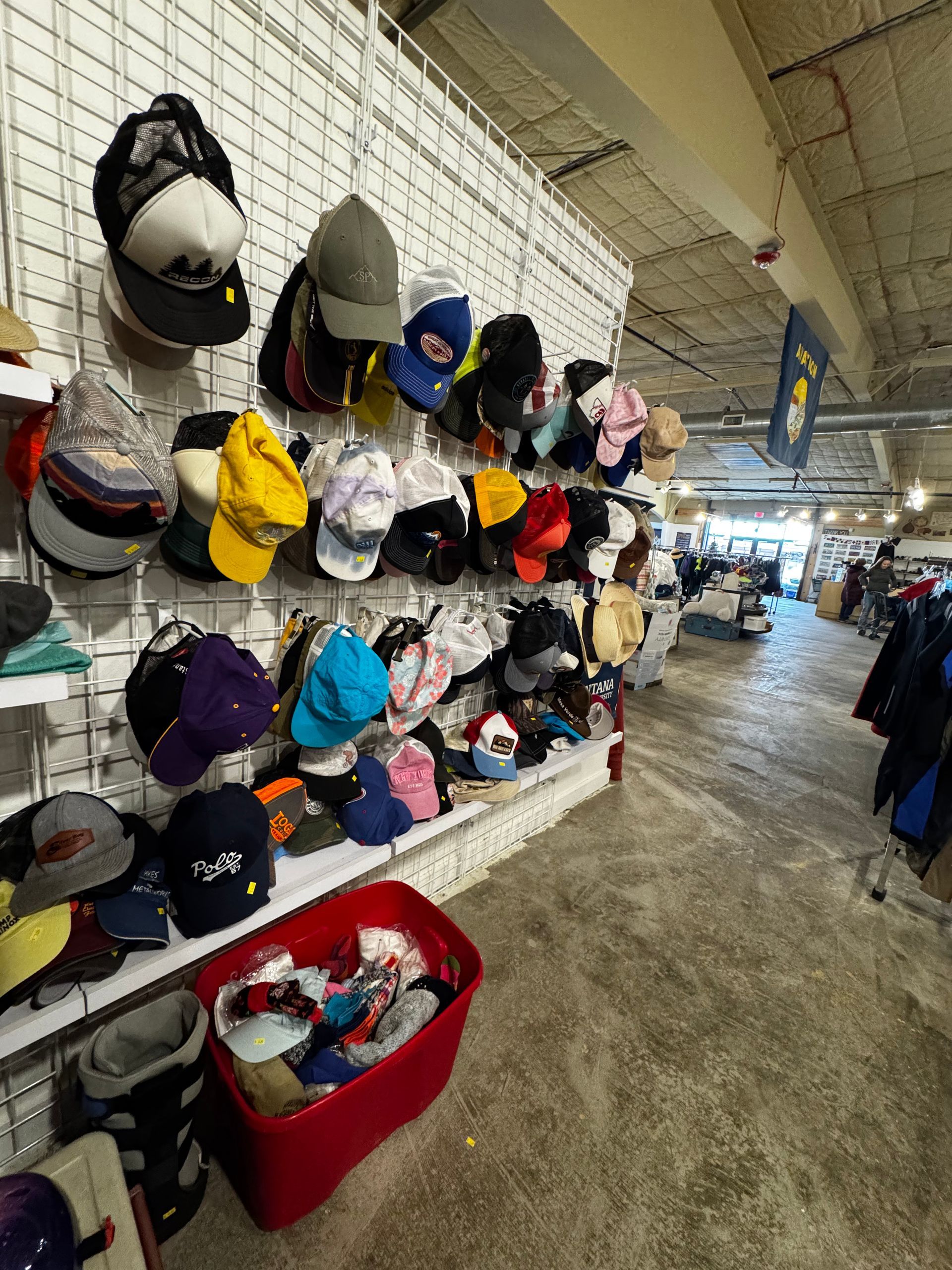 Hats on display at a store, arranged on a white grid wall, with a red bin below filled with clothes.