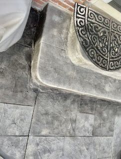A door mat is sitting on a tiled floor next to a brick wall.