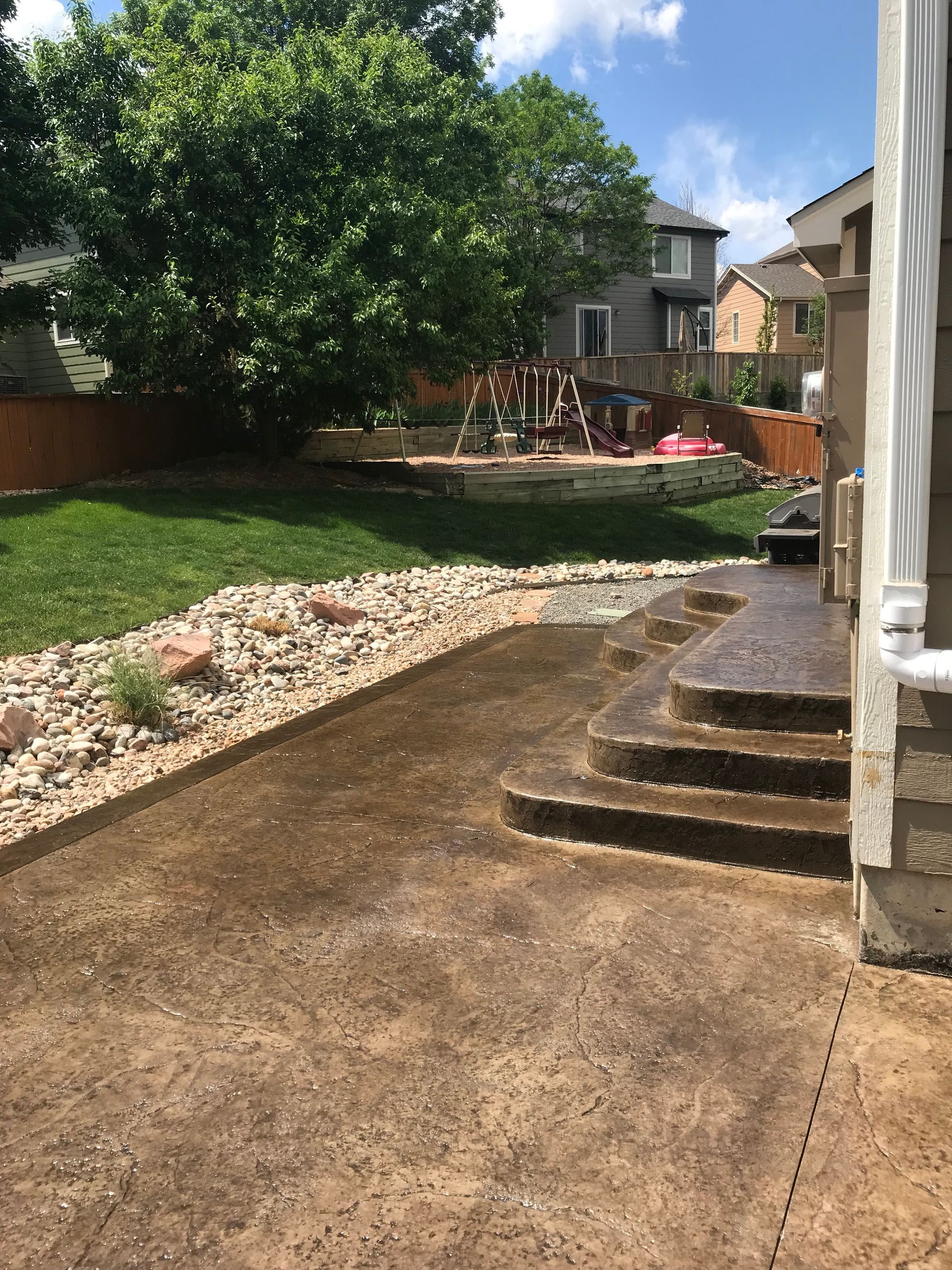 A backyard with a concrete patio and stairs leading up to it.
