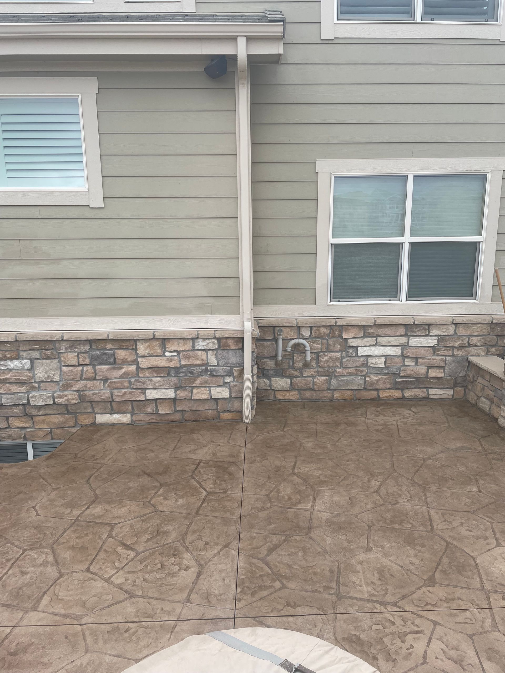 A house with a stone wall and a concrete patio in front of it.