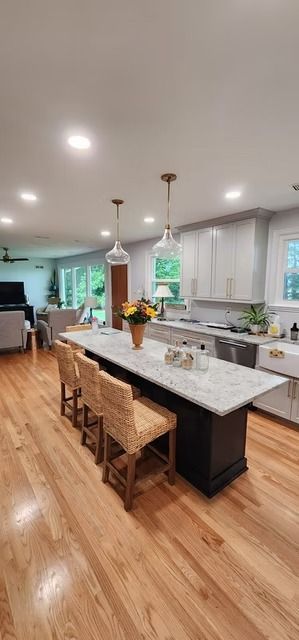 Kitchen with a large island and three wicker bar stools. Light wood floors, white countertops, and gray cabinets create a modern space.