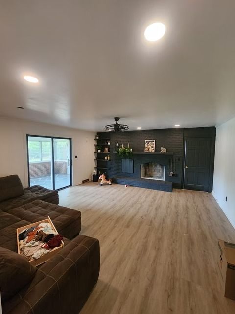 A living room with a brown sectional sofa, dark accent wall with a fireplace, and sliding glass doors leading to an outdoor area.