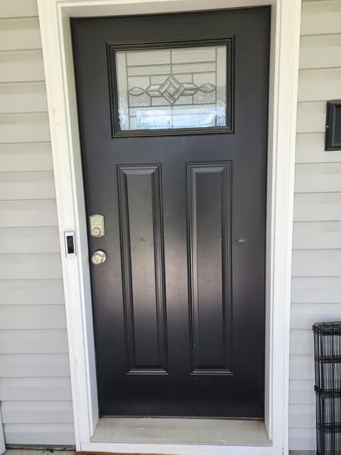 Black front door with a decorative window, set in a white door frame, against gray siding.