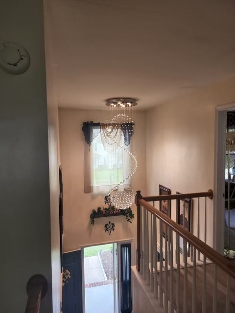 Looking down a staircase with a spiral chandelier. The entryway has a window with blue curtains and wooden railing.