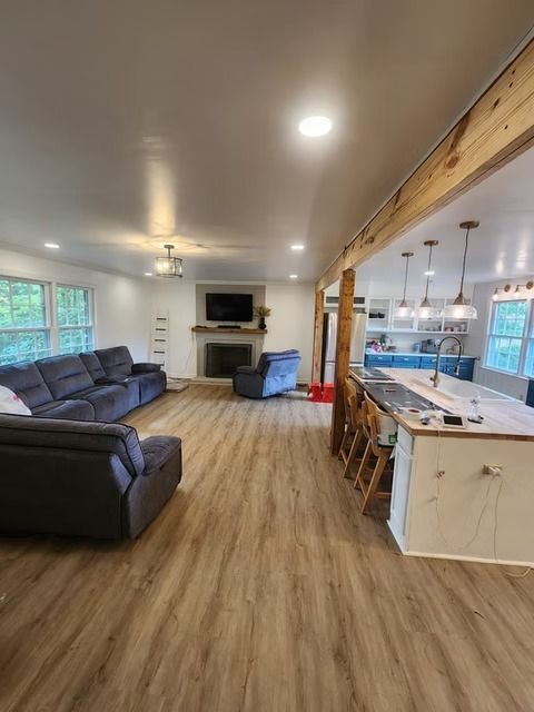 Spacious open-concept living area with wood floors, a gray sectional sofa, a fireplace, and a large kitchen island with bar stools.