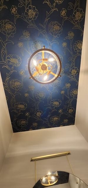 Ceiling with blue floral wallpaper, a circular light fixture, and a golden rod-shaped light below it.