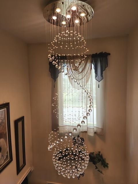 A spiral chandelier with crystal beads hangs in a stairwell. The light fixture has a circular ceiling mount and a large bulbous base.