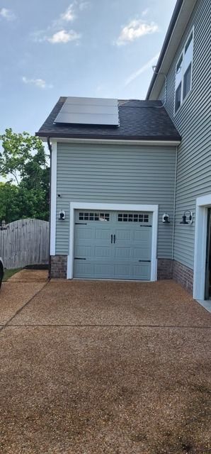 Exterior view of a house with a light blue garage, brown driveway, and solar panels on the roof.