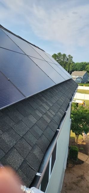 Solar panels installed on a dark-shingled roof with visible gutters. Blue sky visible in the background.