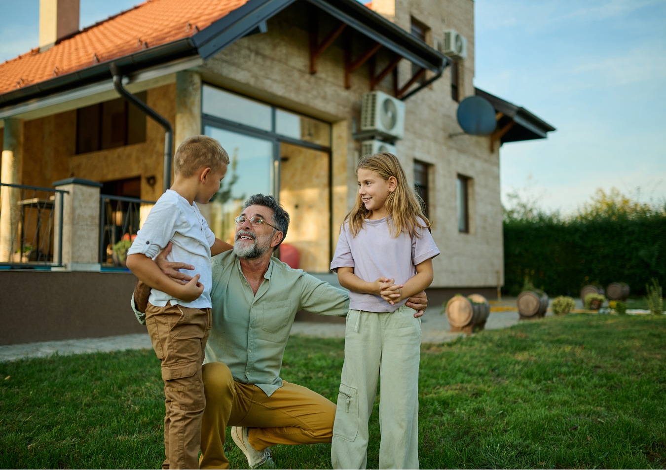 A man is kneeling down with two children in front of a house.