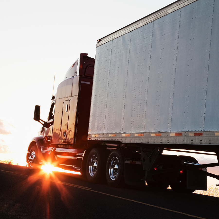 A semi truck is driving down a road with the sun shining on it