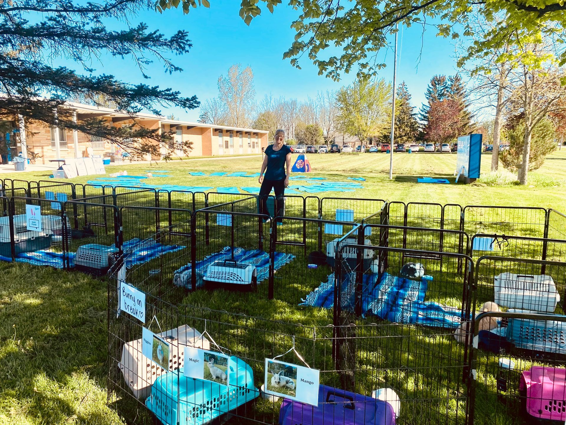 Teacher standing outside the school surrounded by large caged areas for bunnies and yoga mats for children