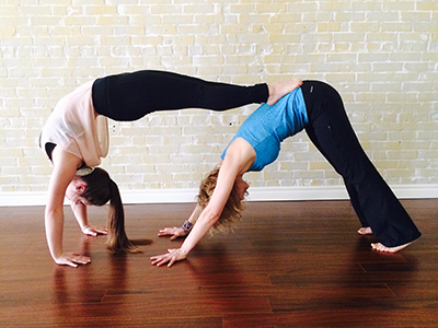 Sheery-Lynne in a downward dog while her daughter does a back bend and rests her feet of her mother's hips