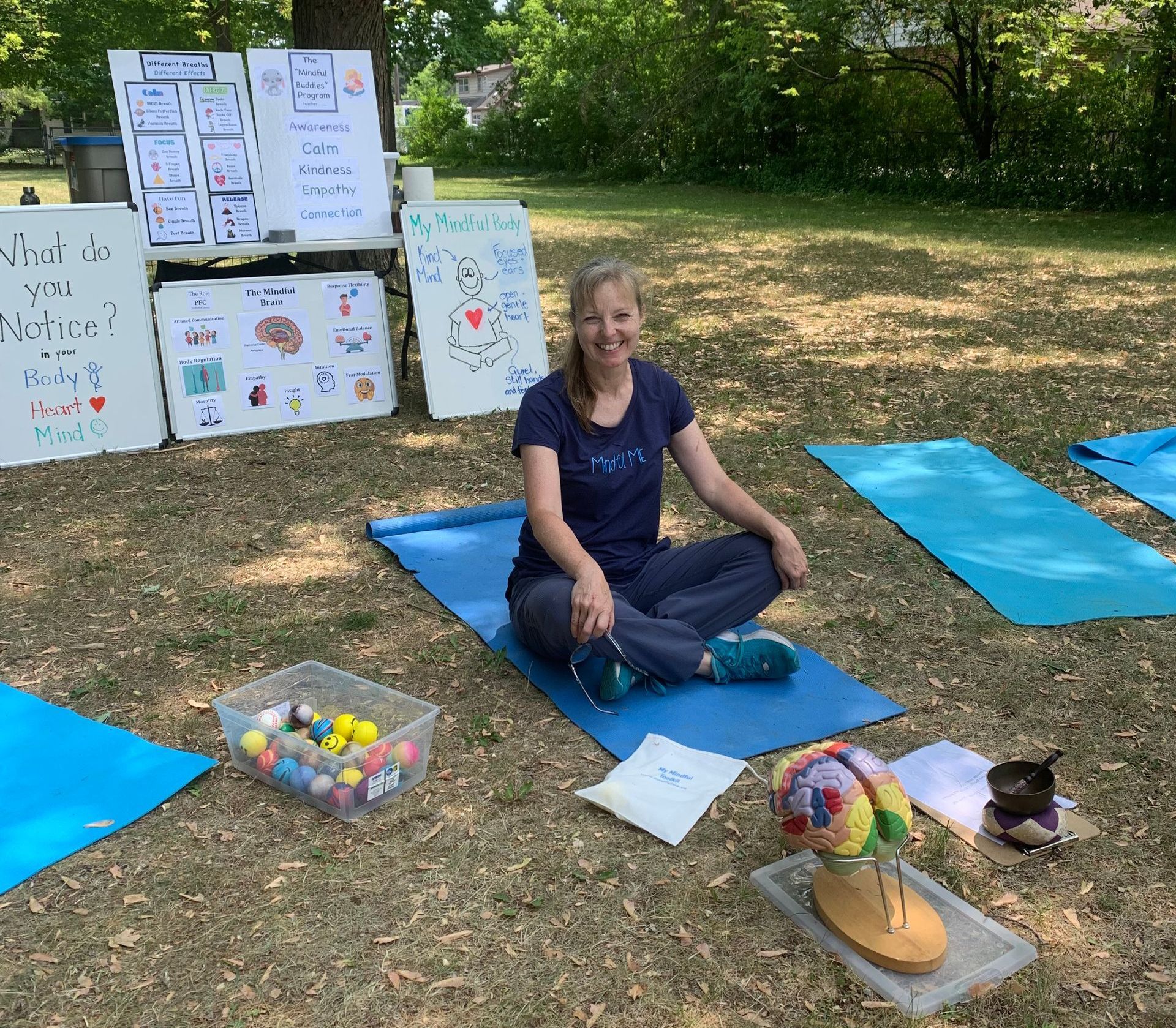 Sherry-Lynne sitting outside ready to teach with yoga mats, a colourful model of the brain, and posters that show mindfulness lessons