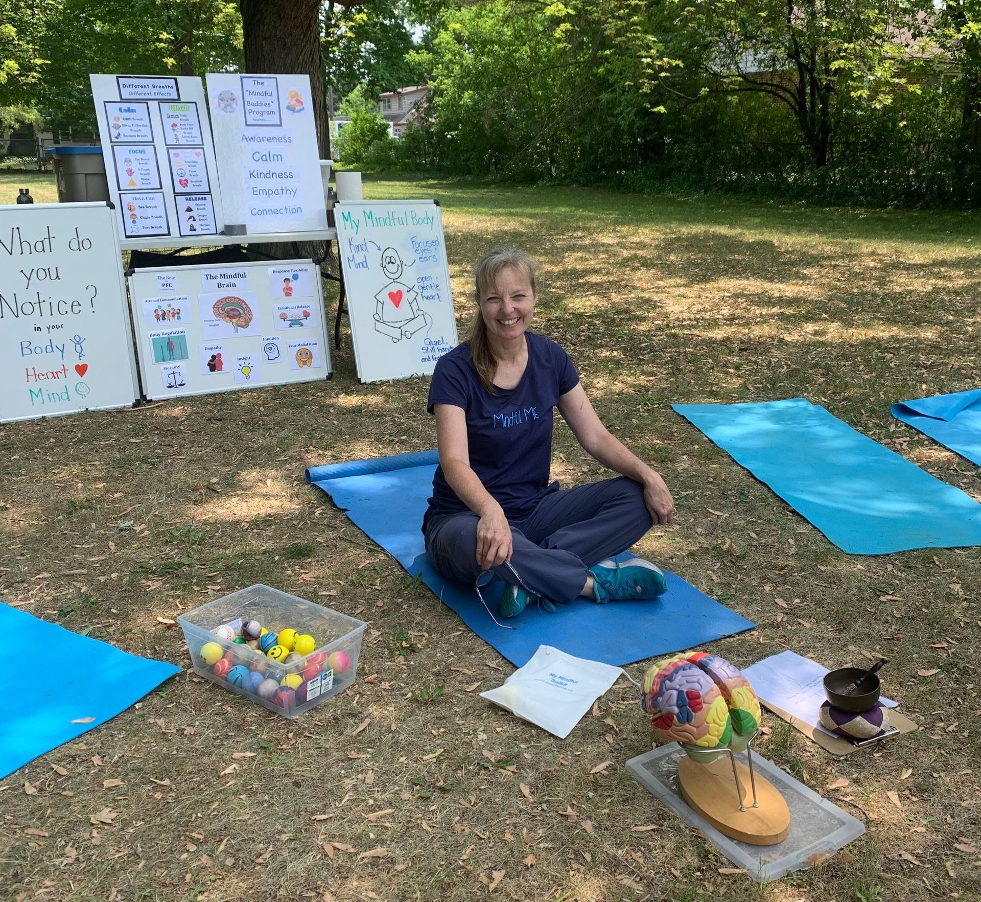 Sherry-Lynne sitting outside ready to teach with yoga mats, a colourful model of the brain, and posters that show mindfulness lessons