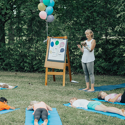 Outdoor children's yoga class with kids on their mats and the teacher standing with a meditation bowl