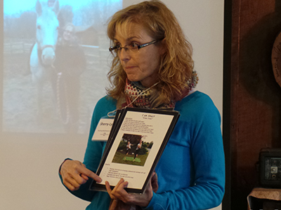 Sheery-Lynne delivering a talk with a slide of a horse in the background