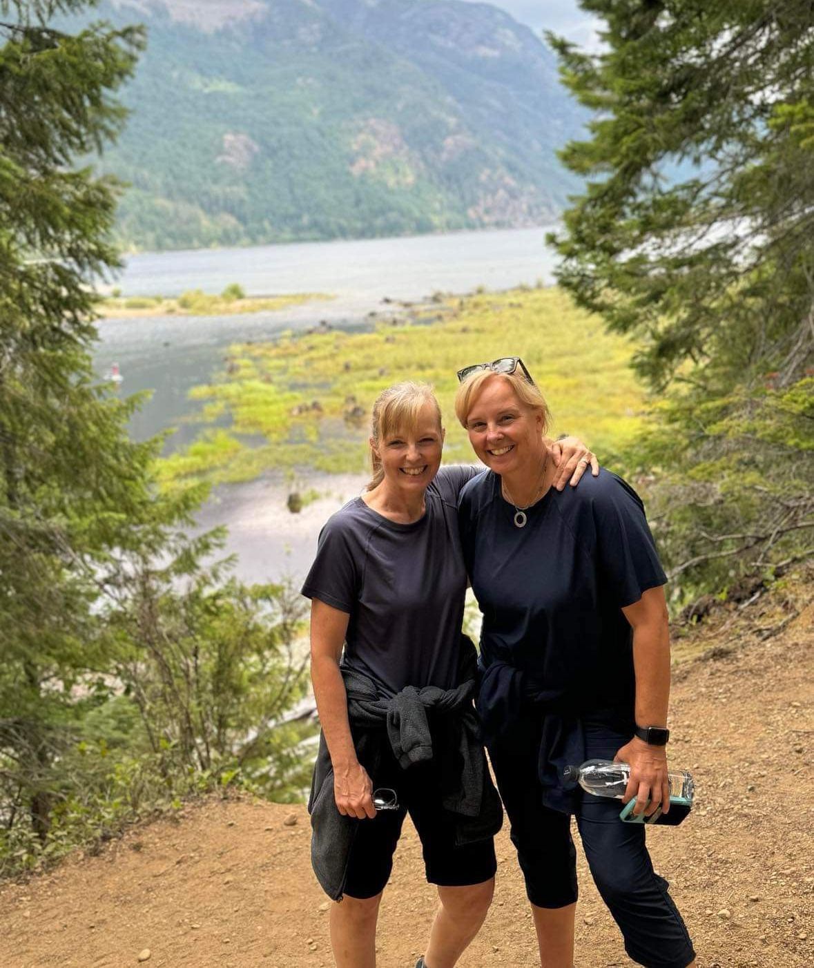 The author standing beside her sister with her left arm wrapped around her shoulder. Both are smiling as they take a break from their hike