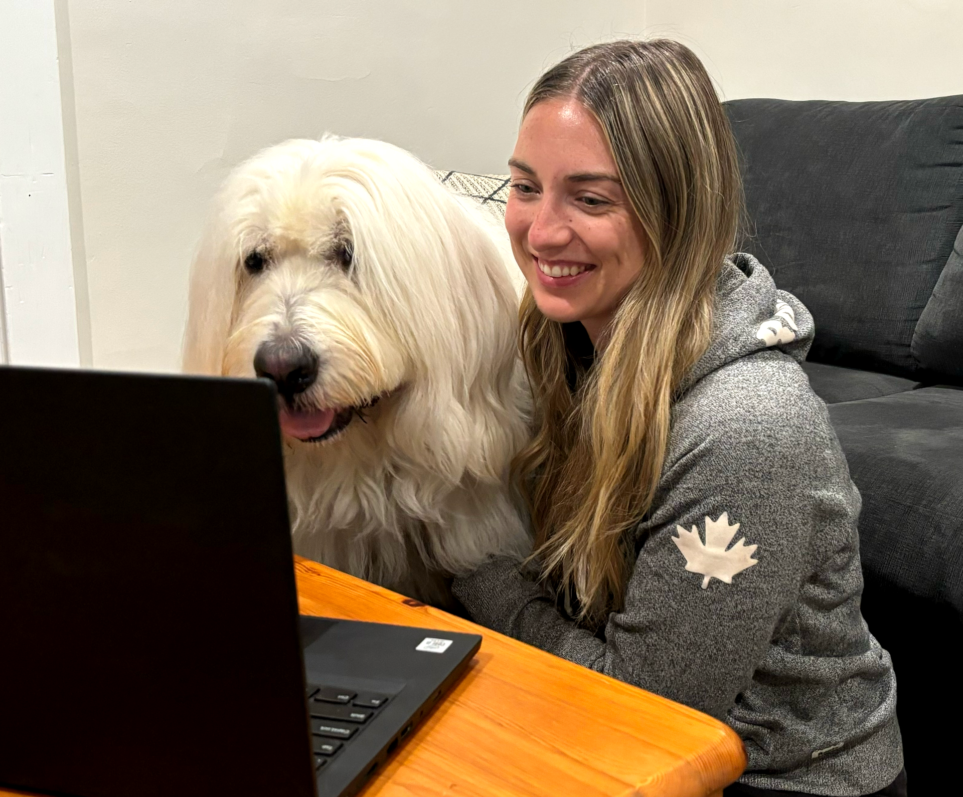 Lady sitting with her dog  as they are watching what's on the screen of their laptop together