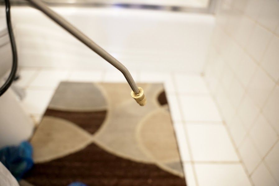 A person is spraying a rug with a sprayer in a bathroom.