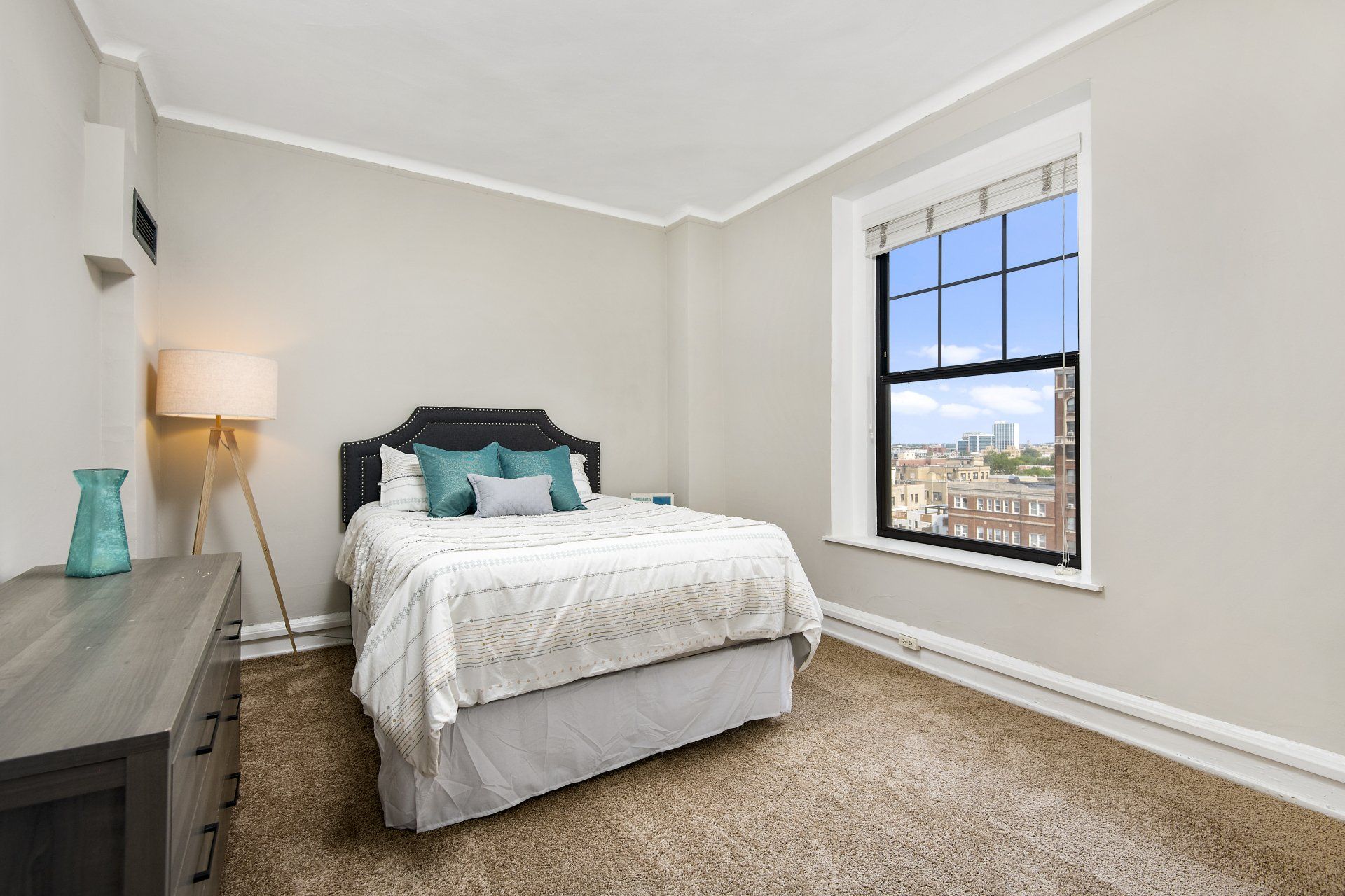 A bedroom with a bed, dresser, lamp, and window at The Belmont by Reside.