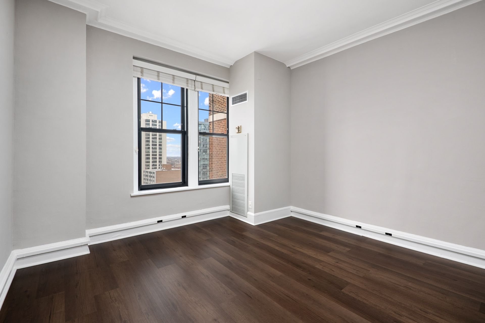 An empty room with hardwood floors and two windows at The Belmont by Reside.