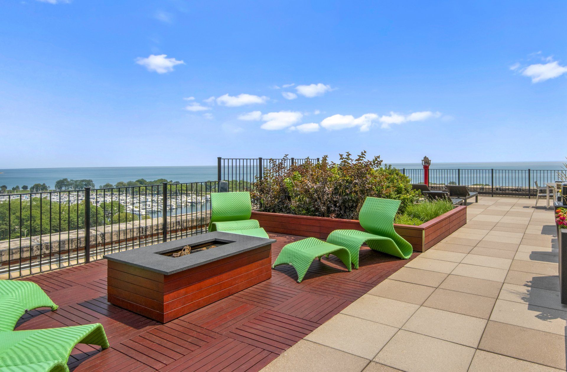 A patio with green chairs and a fire pit overlooking the water at The Belmont by Reside.
