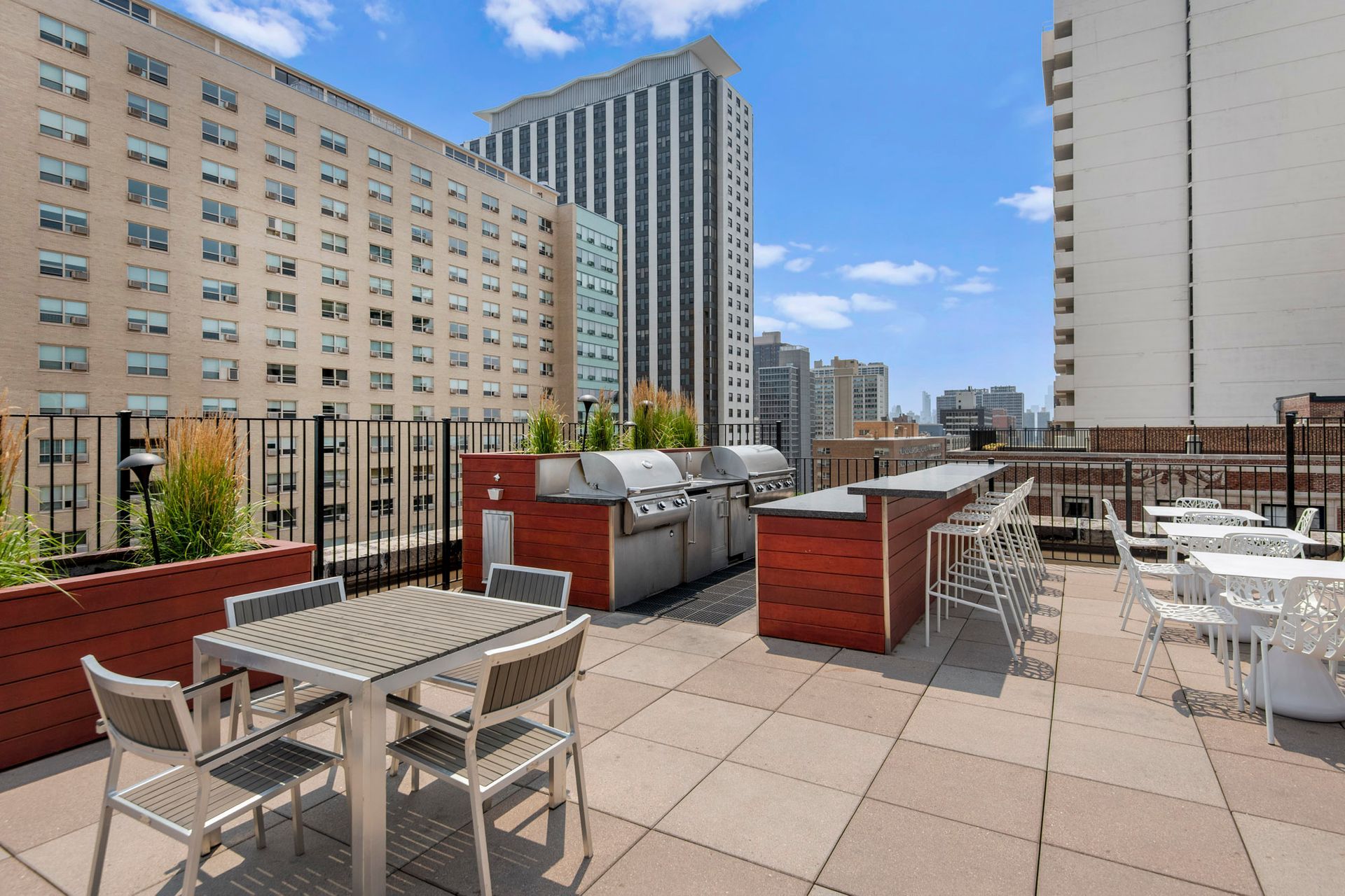 A rooftop patio with tables and chairs and a grill at The Belmont by Reside.