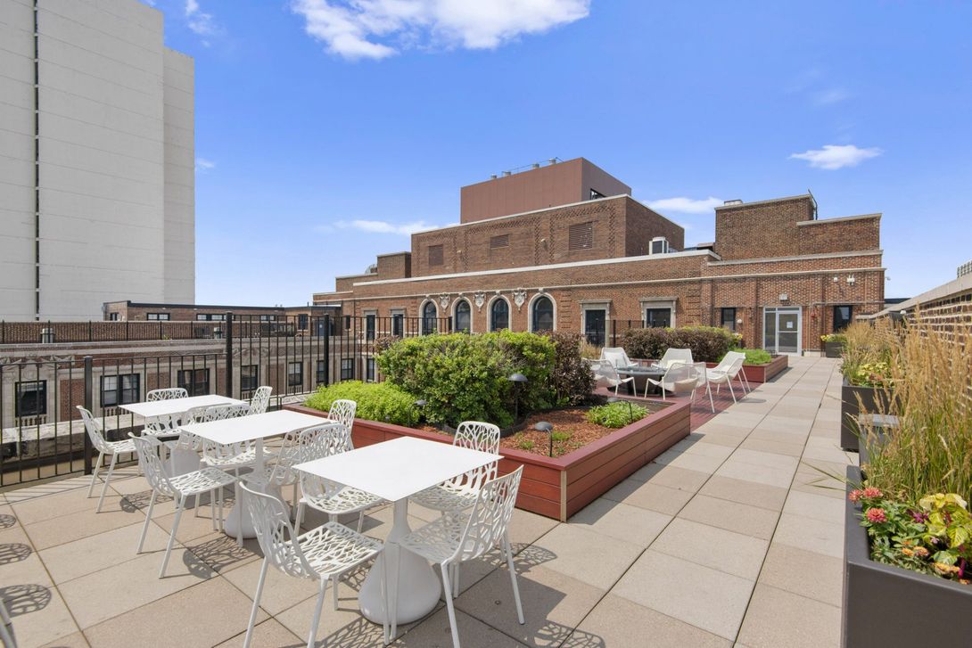 A rooftop patio with tables and chairs and a building in the background at The Belmont by Reside.