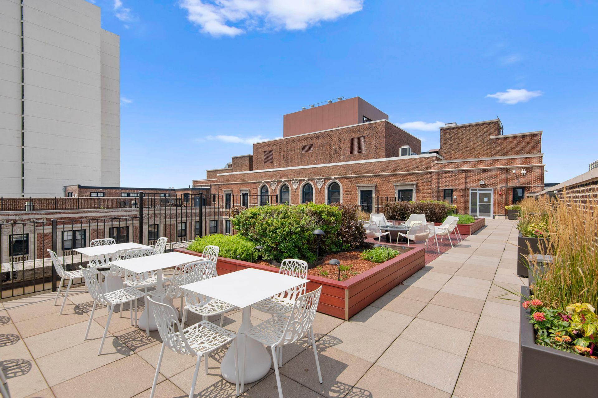A rooftop garden with tables and chairs and a building in the background at The Belmont by Reside.