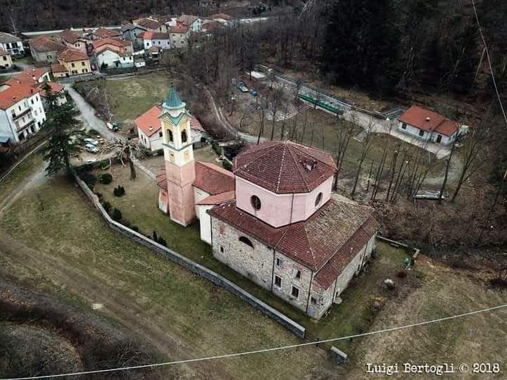 Vista aerea di una chiesa con campanile, circondata da edifici e da un'area erbosa, in un ambiente rurale.