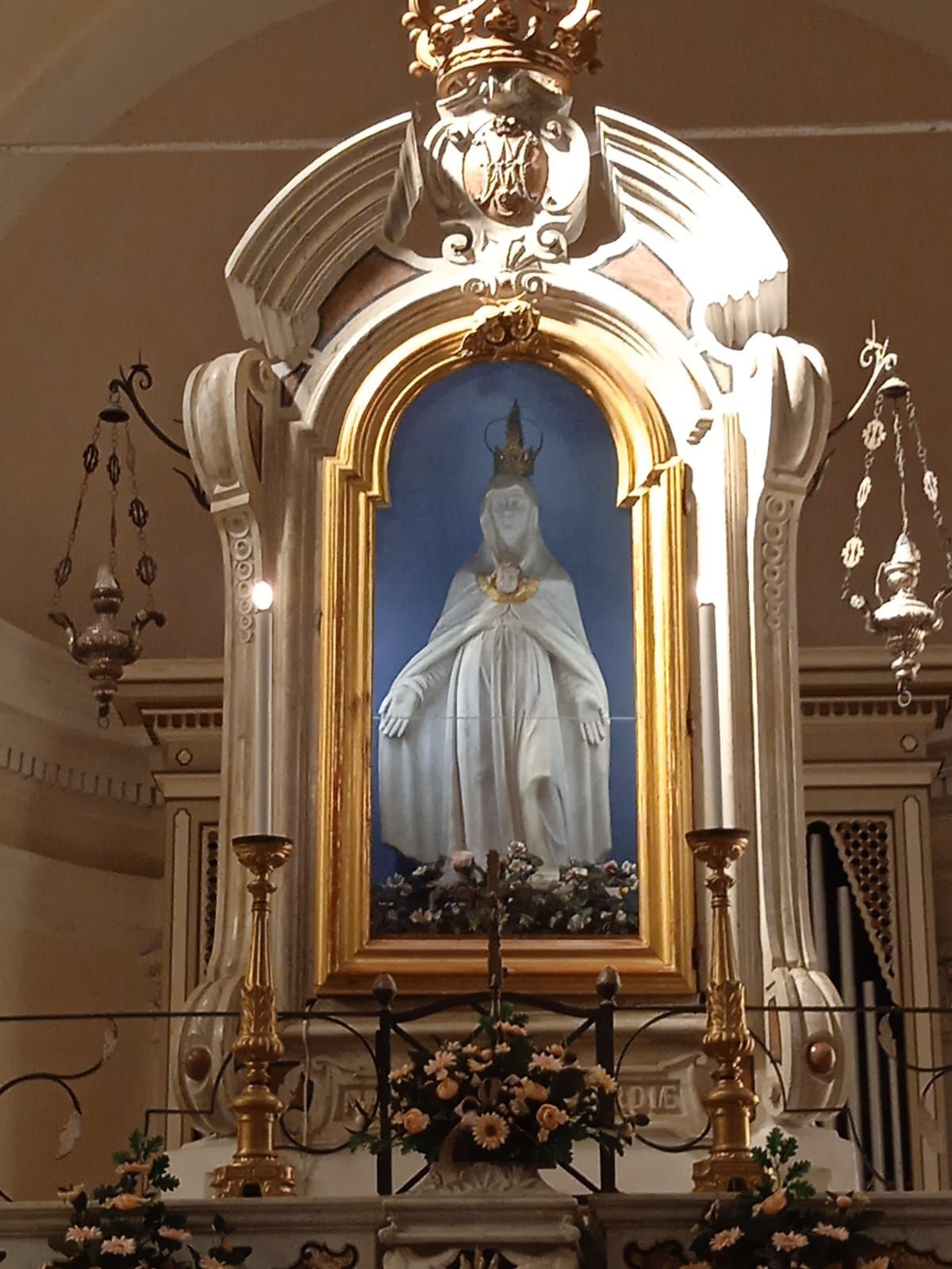 Statua della Vergine Maria in una nicchia della chiesa, con corona e vesti bianche, incorniciata in oro.