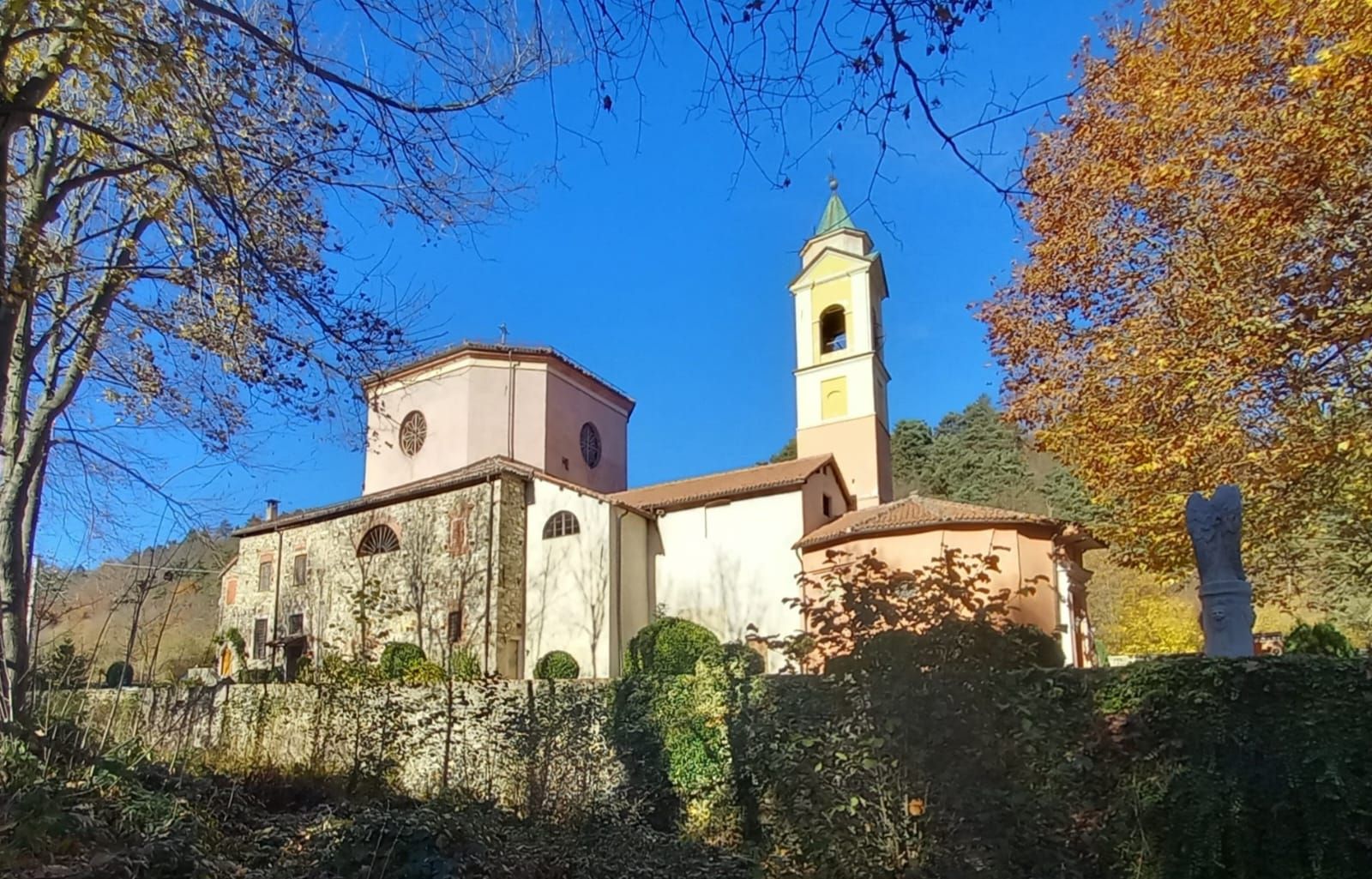 Edificio della chiesa con pareti beige e rosa, campanile e alberi autunnali.